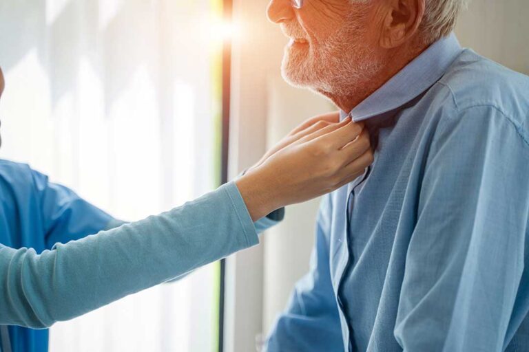 A senior resident talking with a visitor in a bright common room with comfortable chairs and natural light.
